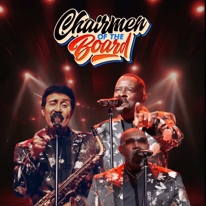 Three men in floral suits sing into microphones on a stage with spotlights in the background, with the "Chairmen of the Board" logo above.