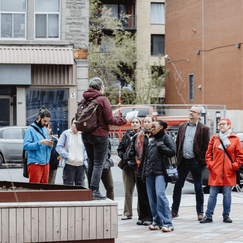 A group of people listen to a guide in front of brick buildings.