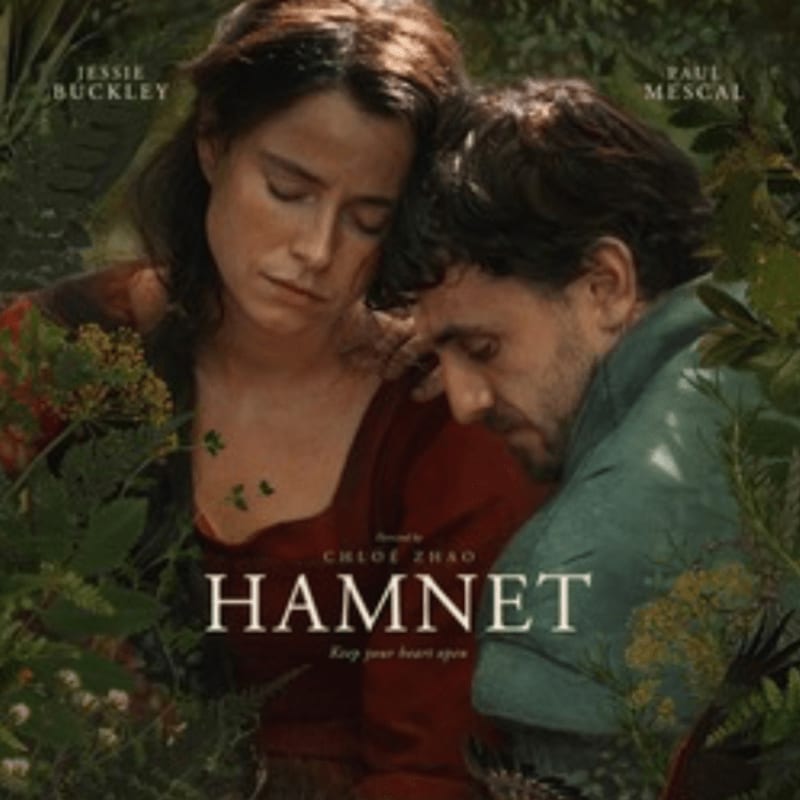 A woman and man embrace tenderly in the foreground, surrounded by lush green foliage in the background.