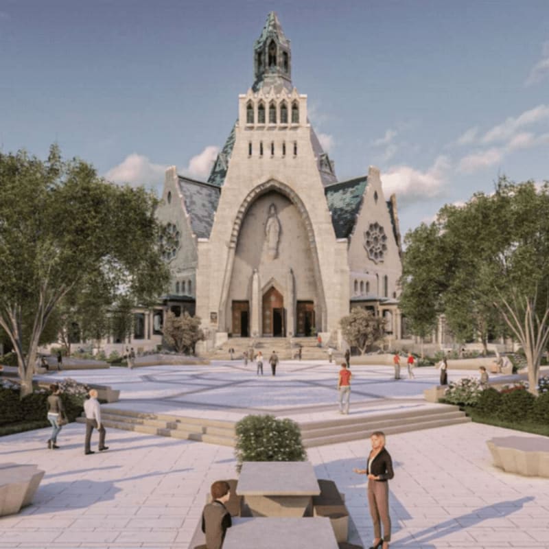 People stroll through a paved plaza with trees and benches in the foreground, leading to a grand stone church with a tall steeple in the background.