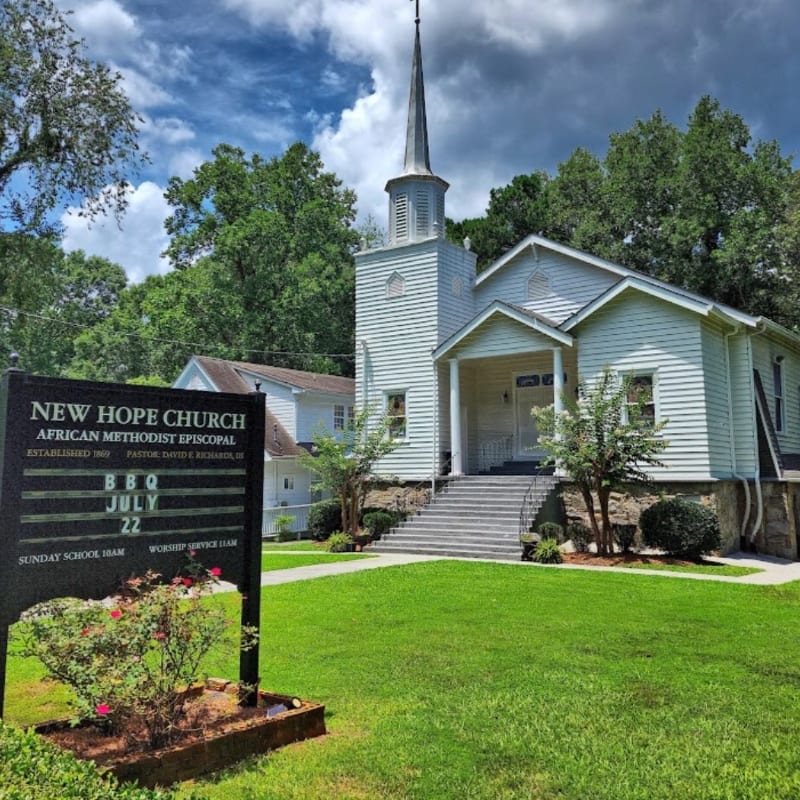 A white church with a steeple stands on a grassy hill in the background, while a sign for "New Hope Church" is in the foreground.