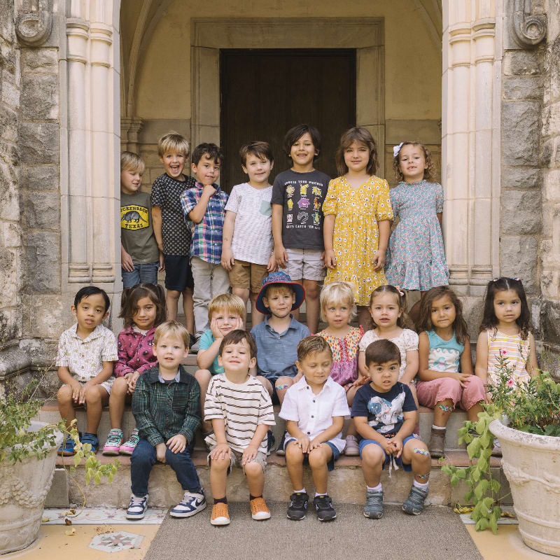 A group of young children pose on stone steps in front of an arched doorway.