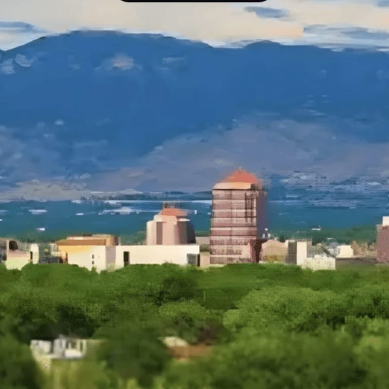 Lush green trees in the foreground frame a cityscape with modern buildings, all set against a backdrop of distant blue mountains under a cloudy sky.