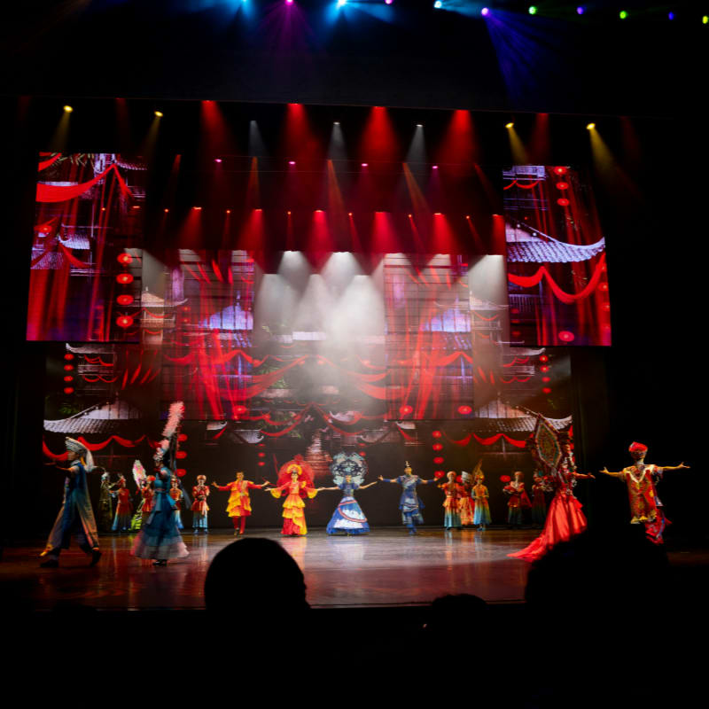 Performers on stage with colorful costumes and backdrop.