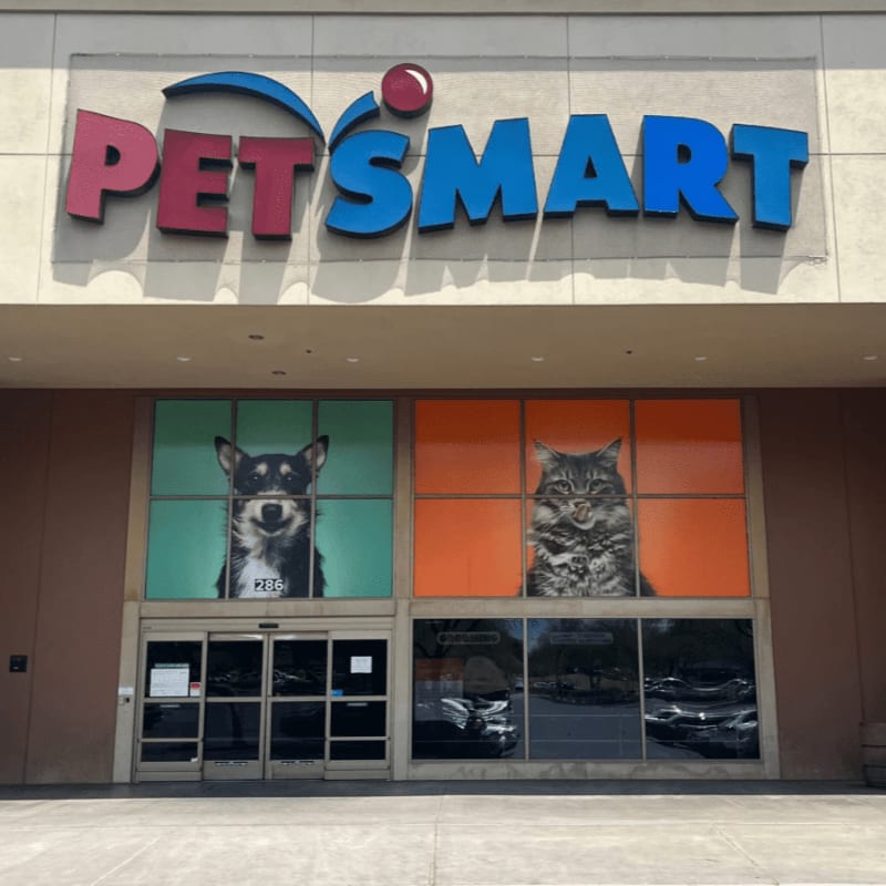 A PetSmart store entrance features large images of a dog and a cat on either side of the doors, with the store's logo above.