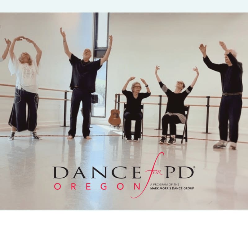 Five individuals, some standing and some seated, are engaged in a dance class with ballet barres and a guitar visible in the background.