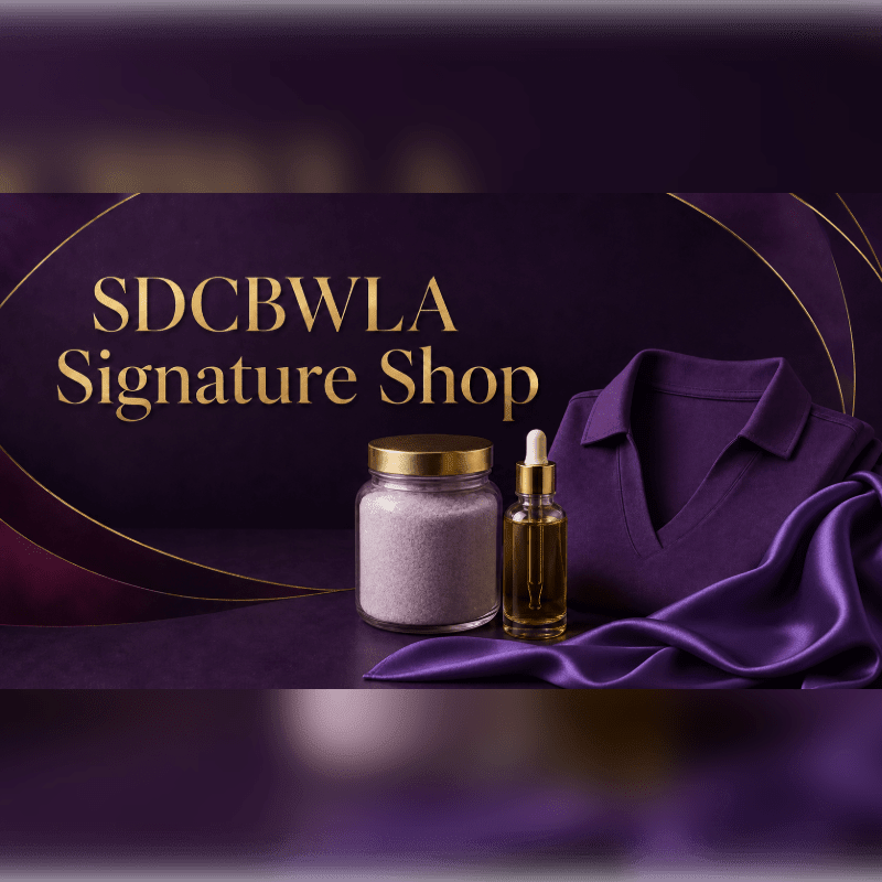 A jar of bath salts and a bottle of serum sit in the foreground on a purple surface, with a folded purple sweater and silk fabric, all set against a dark purple background with gold accents and the text "SDCBWLA Signature Shop."
