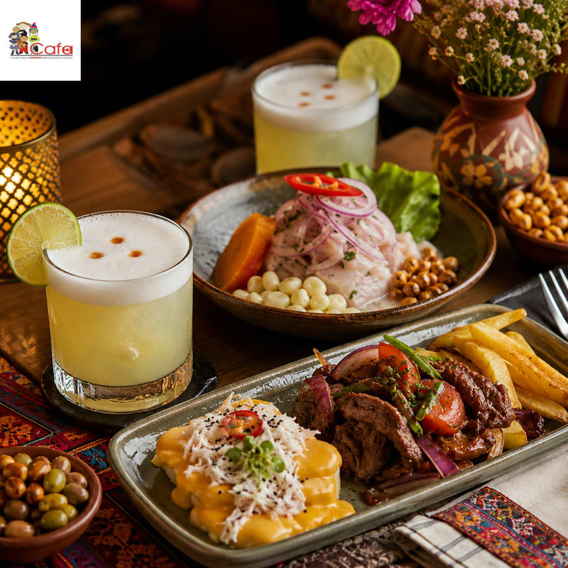 Two pisco sours and a plate of ceviche are in the foreground, with a platter of meat and fries and a vase of flowers in the background.