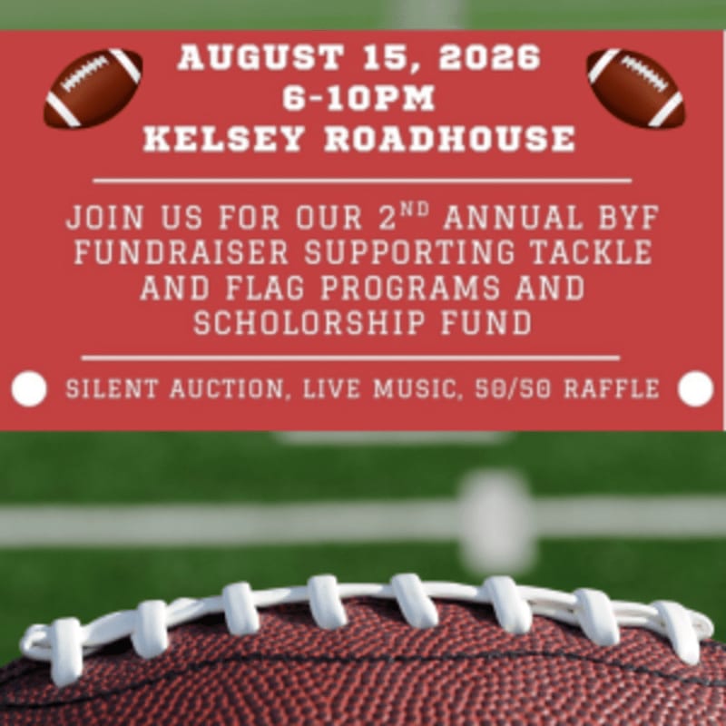 A football rests in the foreground against a red banner advertising a fundraiser, with a blurred green football field in the background.