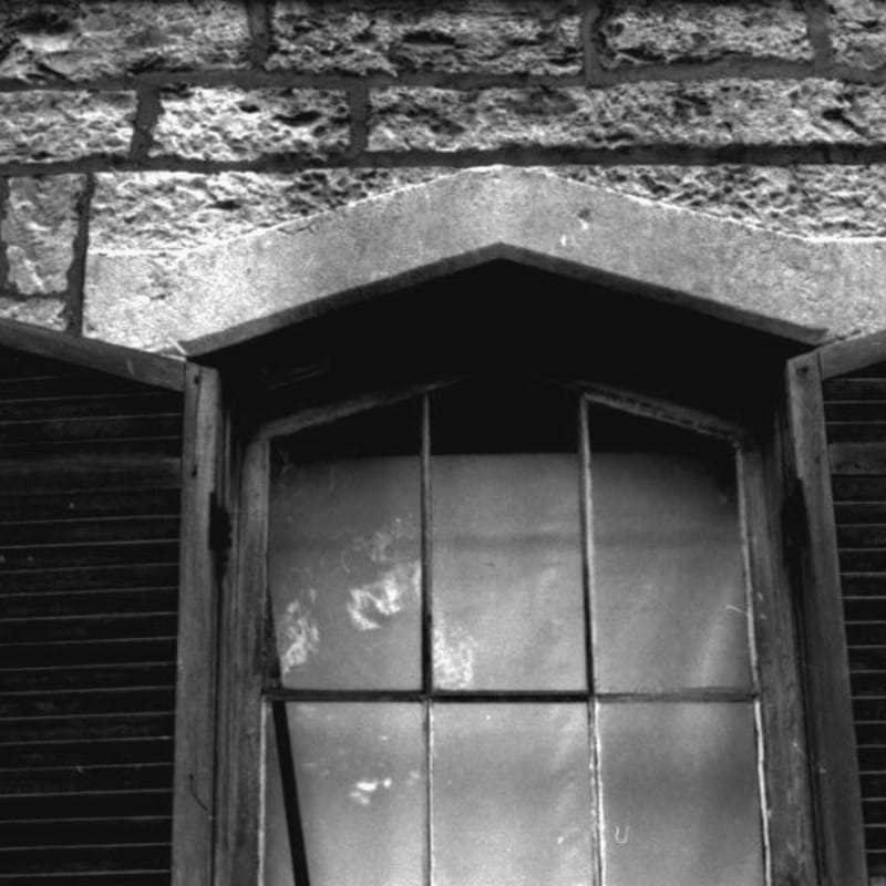 A weathered window with a stone lintel is set against a textured brick wall.
