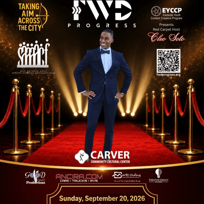 A man in a tuxedo stands on a red carpet with stanchions, while the background features event logos and text.