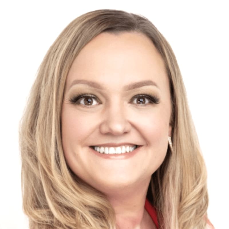 A smiling woman with blonde hair and makeup is in the foreground against a plain white background.