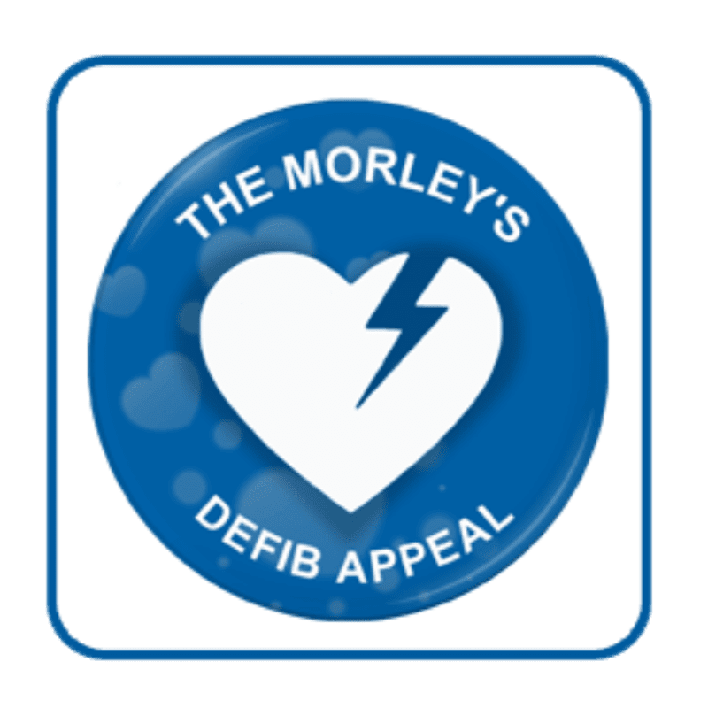 A white heart with a lightning bolt crack is centered on a blue circular background with the words "THE MORLEY'S DEFIB APPEAL" around it, set against a white square with rounded corners and a faint pattern of hearts.