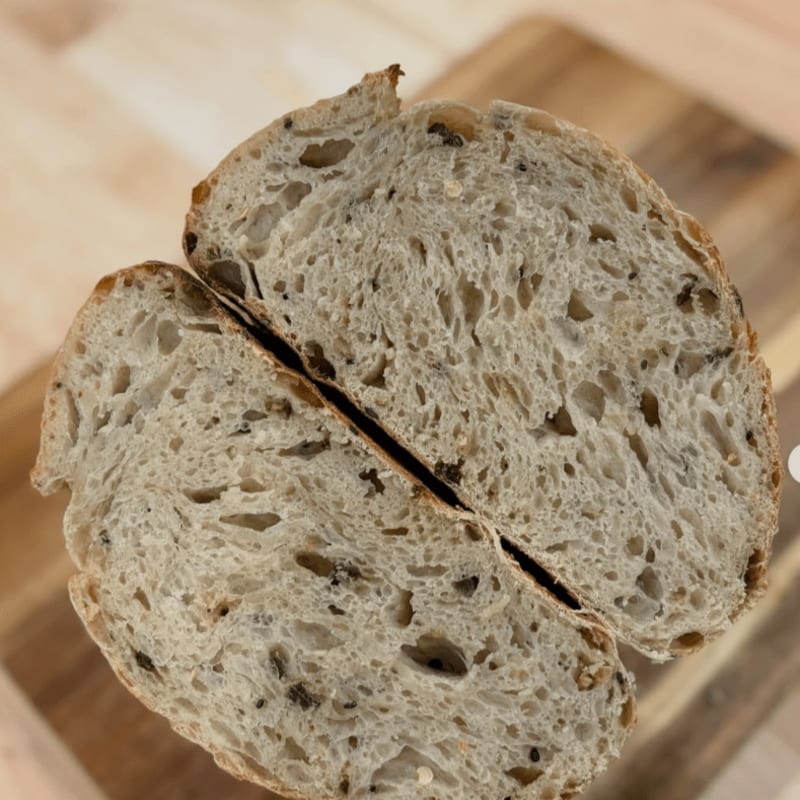 A rustic loaf of bread, sliced in half to reveal its airy crumb and inclusions, rests on a wooden cutting board.