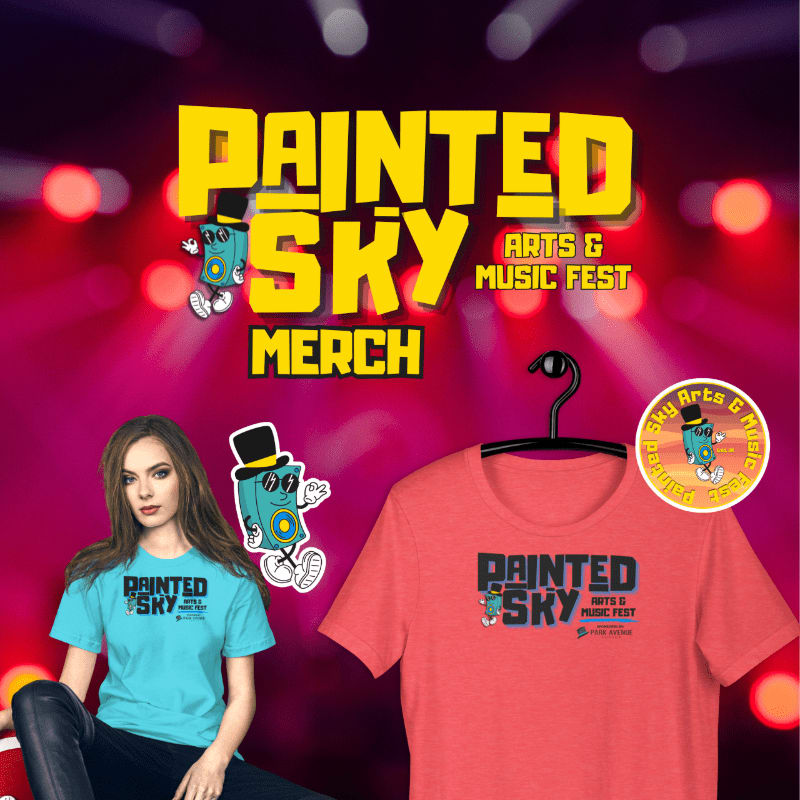 A woman in a blue t-shirt stands in front of a coral t-shirt on a hanger, both displaying "Painted Sky Arts & Music Fest" merchandise, against a blurred background of stage lights.