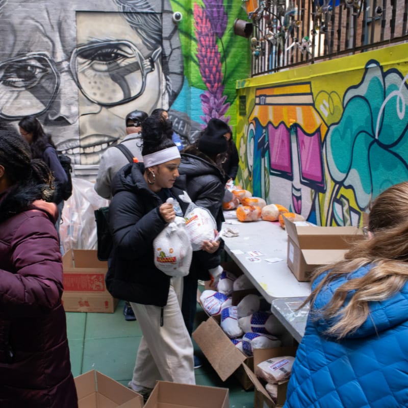 People are collecting food items from a table set up against a vibrant mural-covered wall.