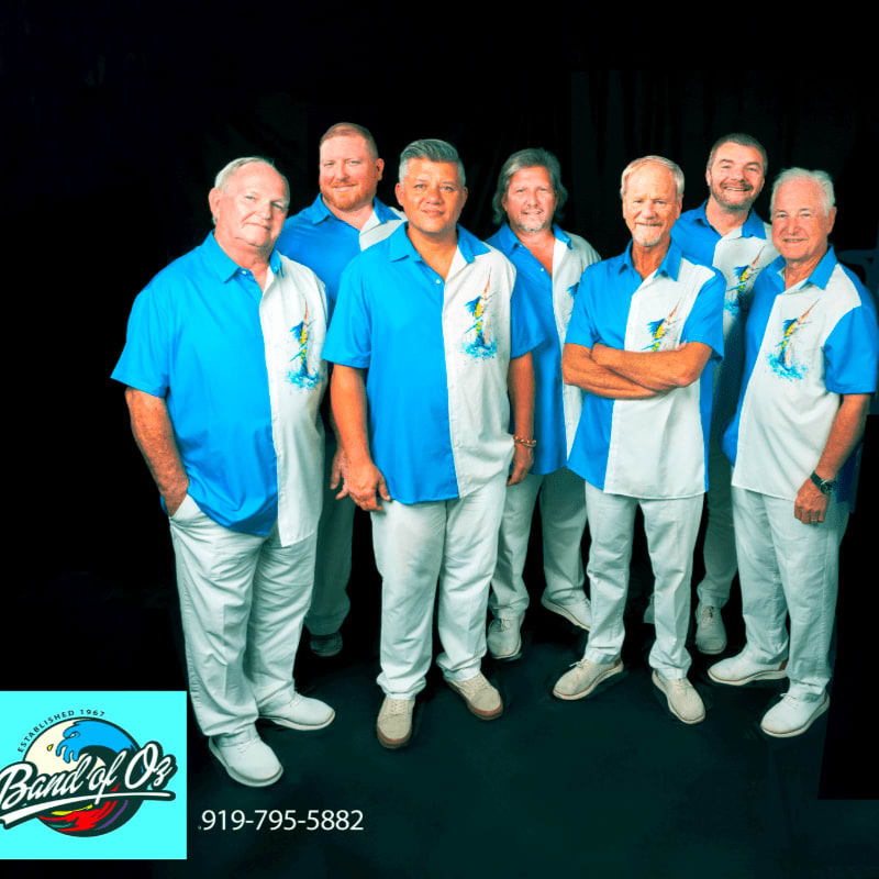 Seven men in matching blue and white shirts and white pants stand in the foreground against a dark background, with a logo and phone number in the lower left corner.