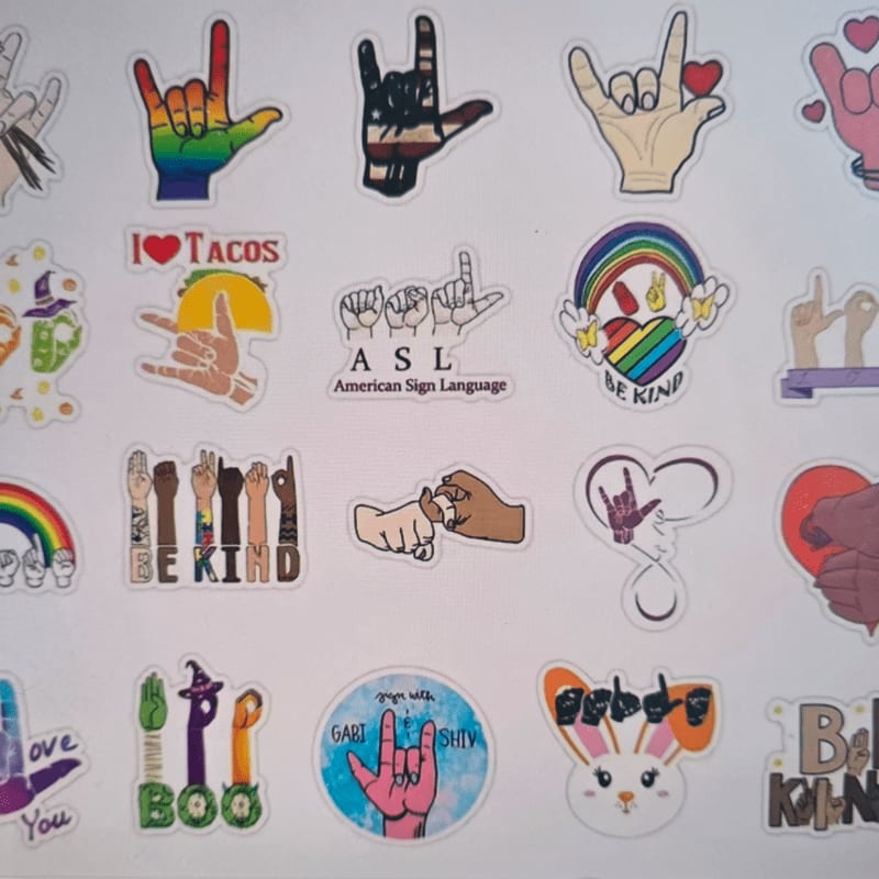 A collection of colorful stickers featuring various hand gestures, rainbows, and positive messages like "BE KIND" and "I ❤️ TACOS" are arranged on a white background.
