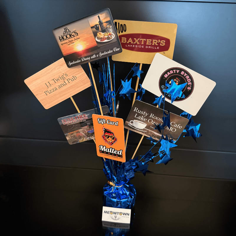 A bouquet of restaurant gift cards, including JB Hooks, Baxter's Lakeside Grille, and J.J. Twig's Pizza and Pub, is arranged in a blue vase against a dark background.