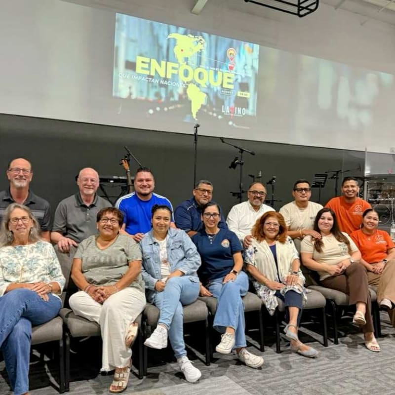 A group of people are seated in chairs in the foreground, with a large screen displaying "ENFOQUE" in the background.