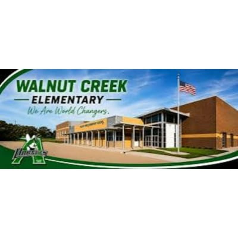 A modern elementary school building with a flagpole in front stands against a bright blue sky with clouds.