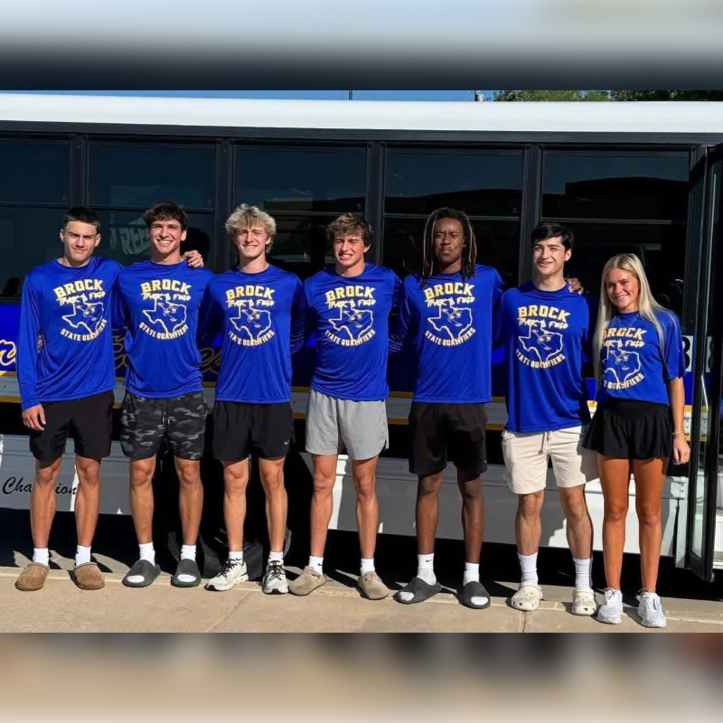 Seven young athletes in blue "Brock State Champions" shirts and athletic shorts stand in front of a bus.