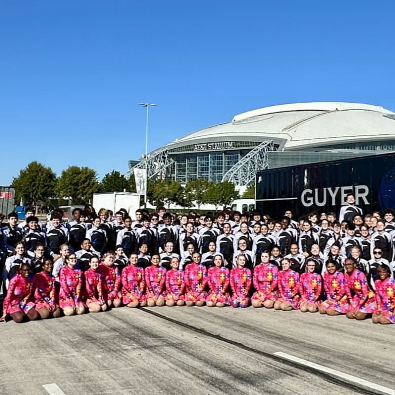 A large group of students in matching uniforms pose in front of a stadium and a large truck.