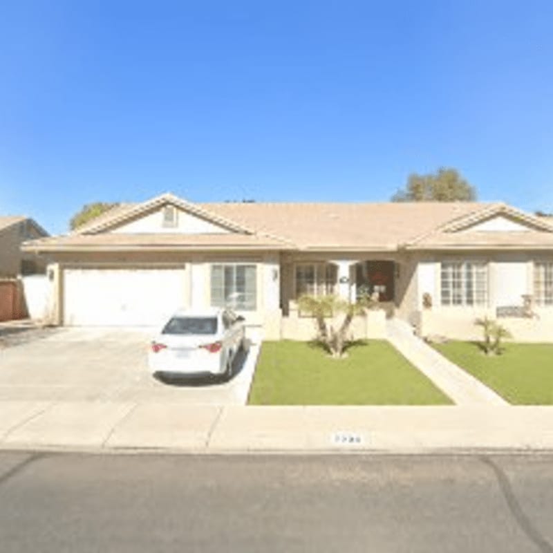 A white car is parked in the driveway of a beige ranch-style house with a well-maintained lawn, set against a clear blue sky.