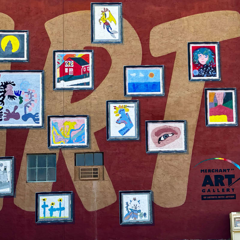 Colorful framed artworks are displayed on a textured red wall with a large "ART" graphic in the background.