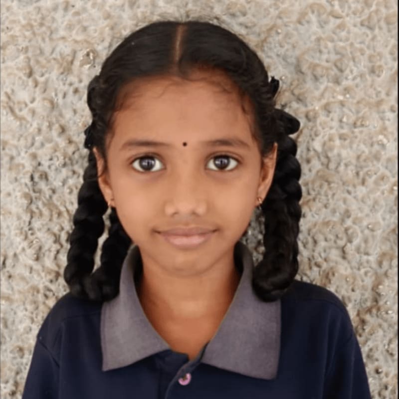A young girl with braided hair and a dark blue shirt stands in front of a textured, light-colored wall.