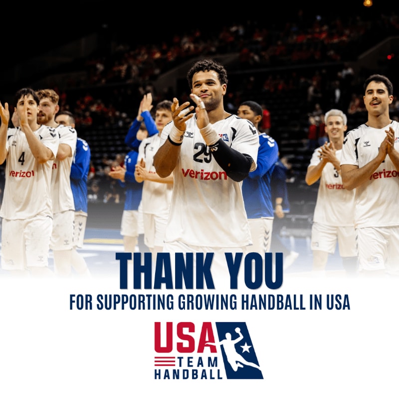 A group of male handball players in white uniforms clap their hands in the foreground, with a blurred stadium crowd visible in the background.