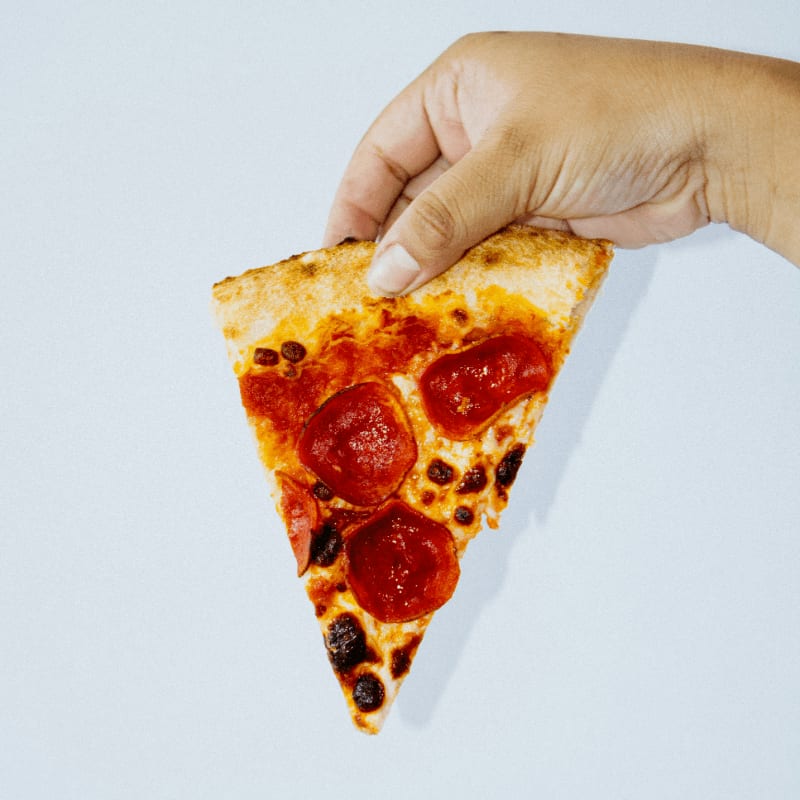 a hand holding a slice of pizza with pepperoni on it