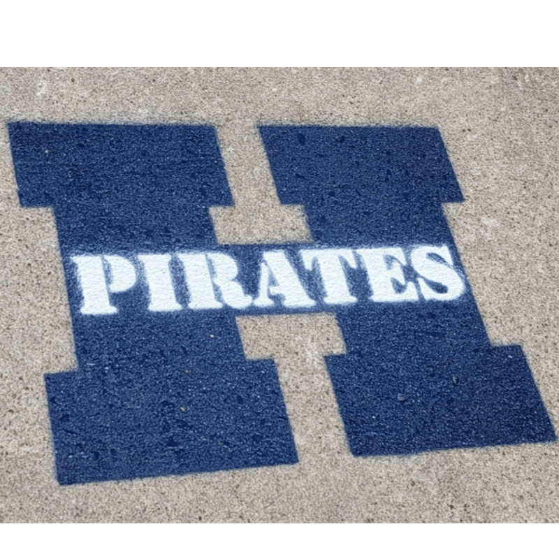 A large blue "H" with "PIRATES" written in white across its center is stenciled onto a textured concrete surface.