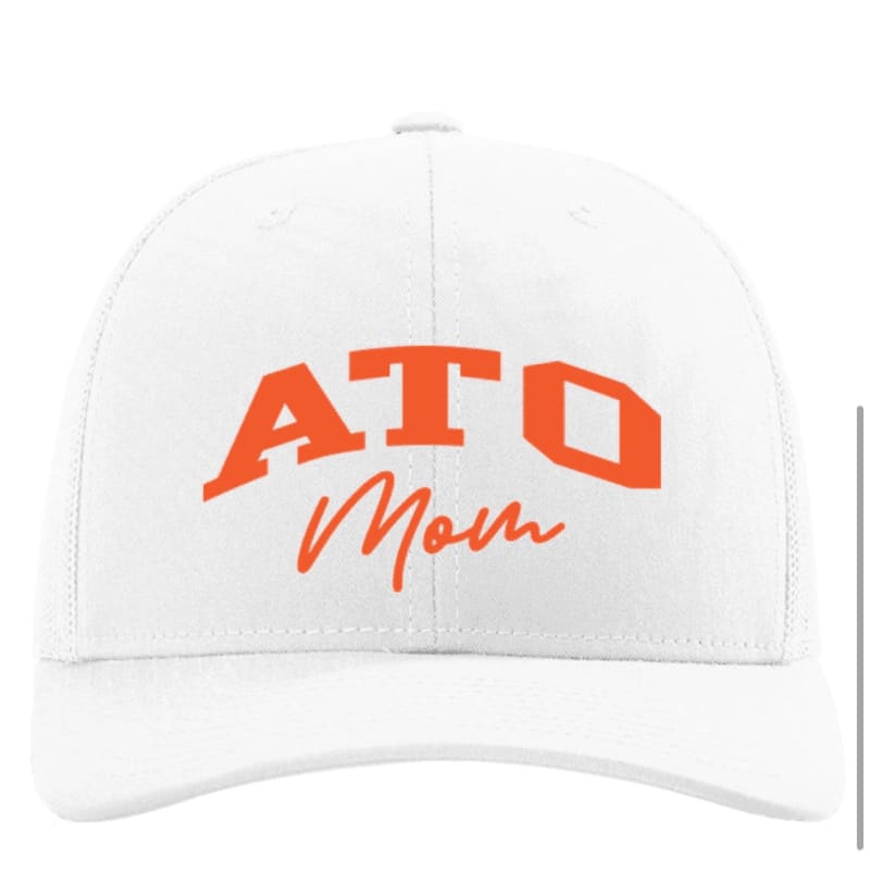 A white baseball cap with orange lettering that says "ATO Mom" is displayed against a plain white background.