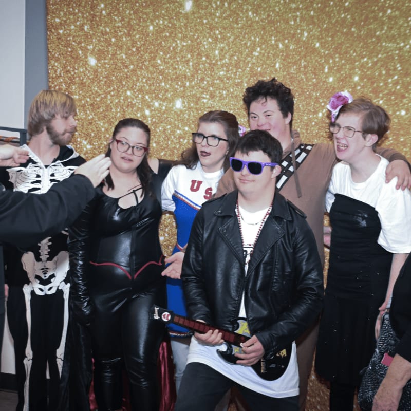 A group of people in costumes pose in front of a sparkling gold background.