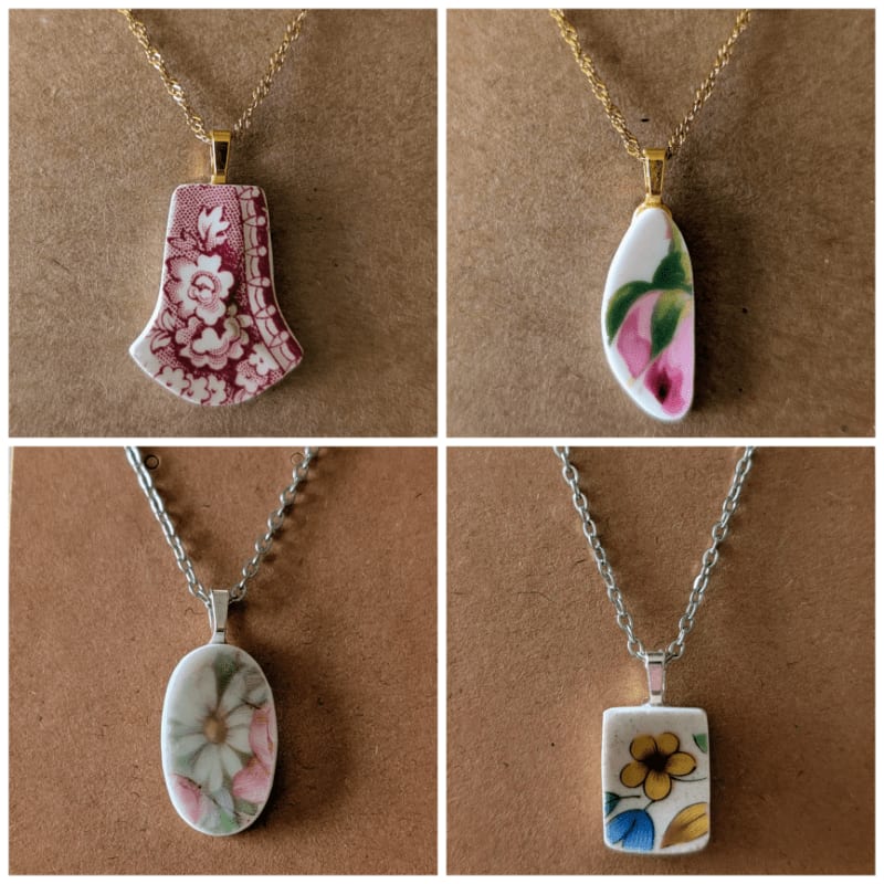 Four unique ceramic shard pendants with floral designs hang on delicate chains against a textured brown background.