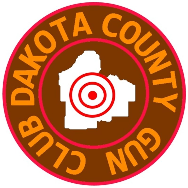 A white outline of a county with a red bullseye is centered within a brown circular emblem that reads "Dakota County Gun Club" in orange lettering.