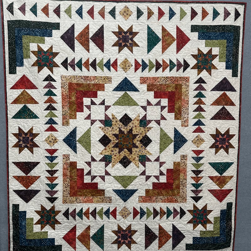 A detailed quilt with a central starburst design is surrounded by a pattern of triangles and corner blocks, all set against a plain background.