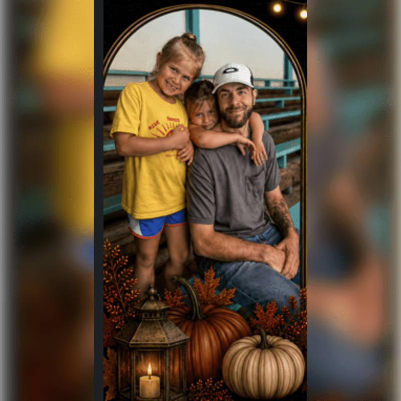 A father and his two daughters smile in front of bleachers, with a lantern and pumpkins in the foreground.