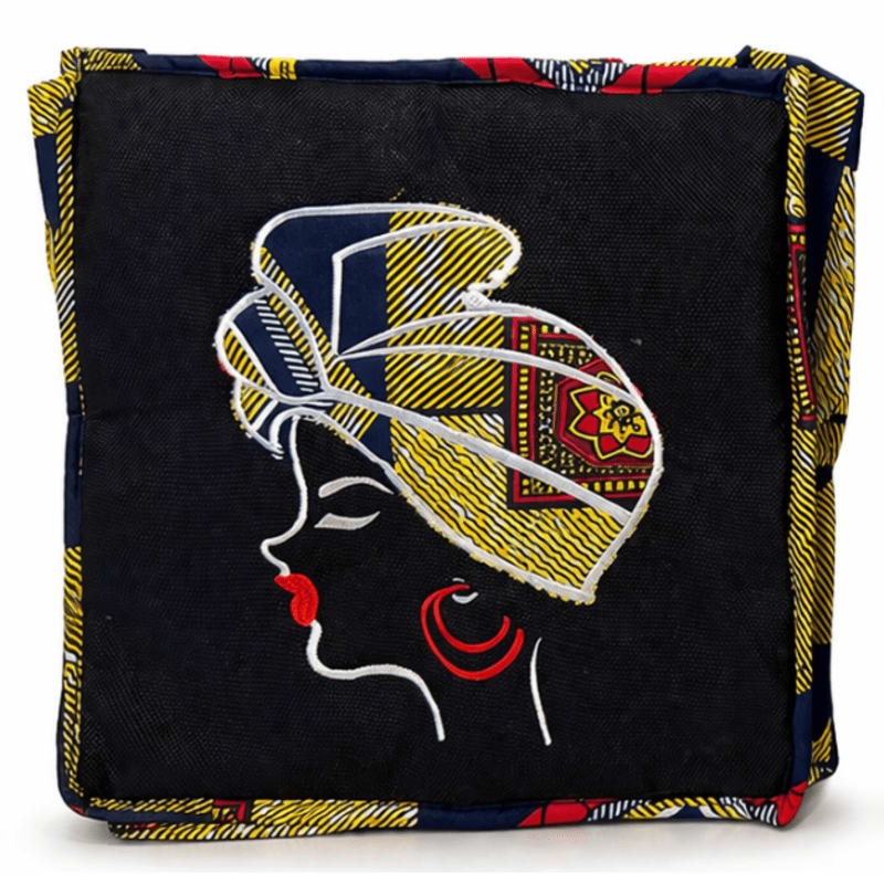 A black cube with an embroidered profile of a woman wearing a colorful headwrap and hoop earrings is surrounded by a vibrant, patterned fabric.