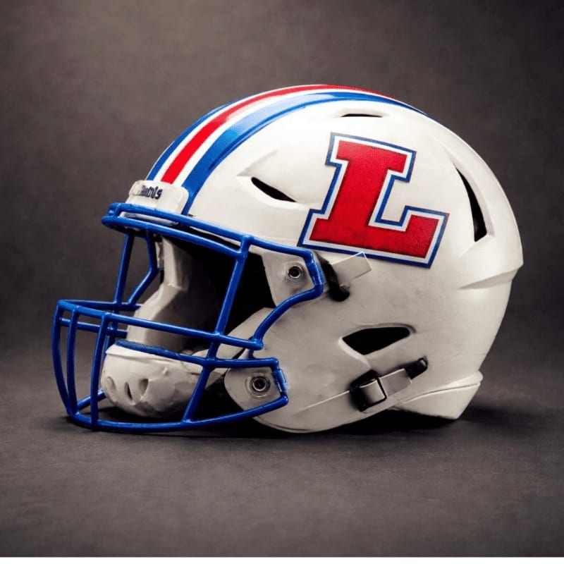 A white football helmet with red and blue stripes and a red "L" logo sits on a dark gray surface against a dark gray background.