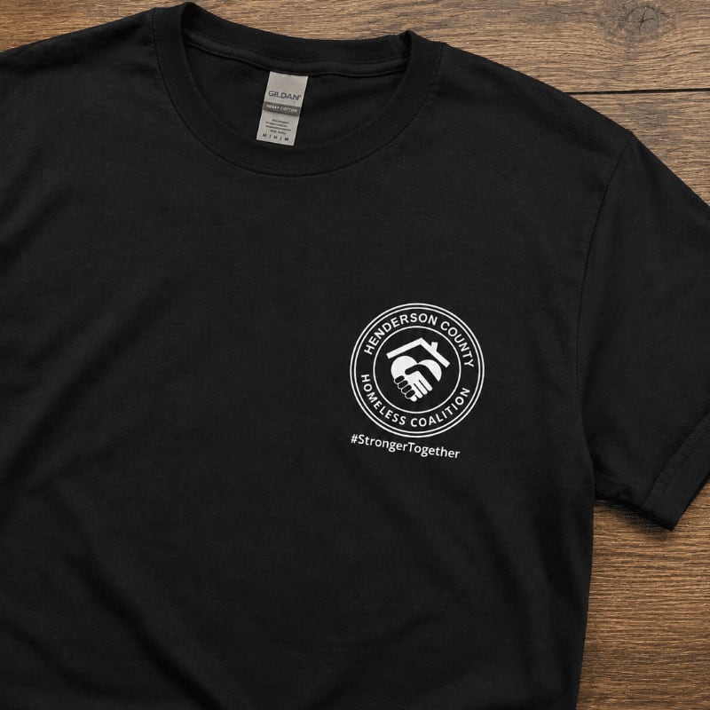 A black t-shirt with a white circular logo and hashtag is laid out on a wooden surface.