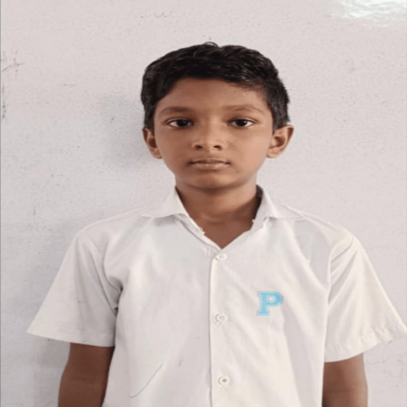 A young boy in a white collared shirt stands against a plain, textured wall.