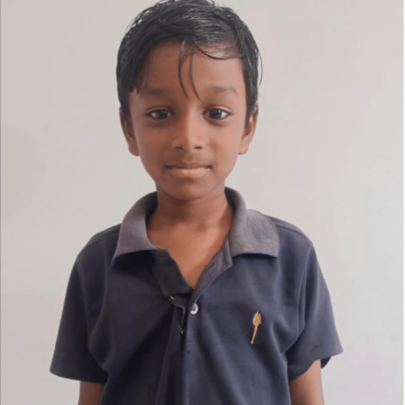 A young boy in a dark blue polo shirt stands against a plain, light-colored background.