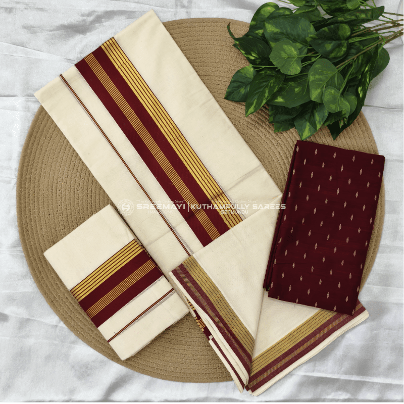 A cream-colored dhoti and matching fabric with maroon and gold stripes are arranged on a woven mat, with a leafy green plant in the background.