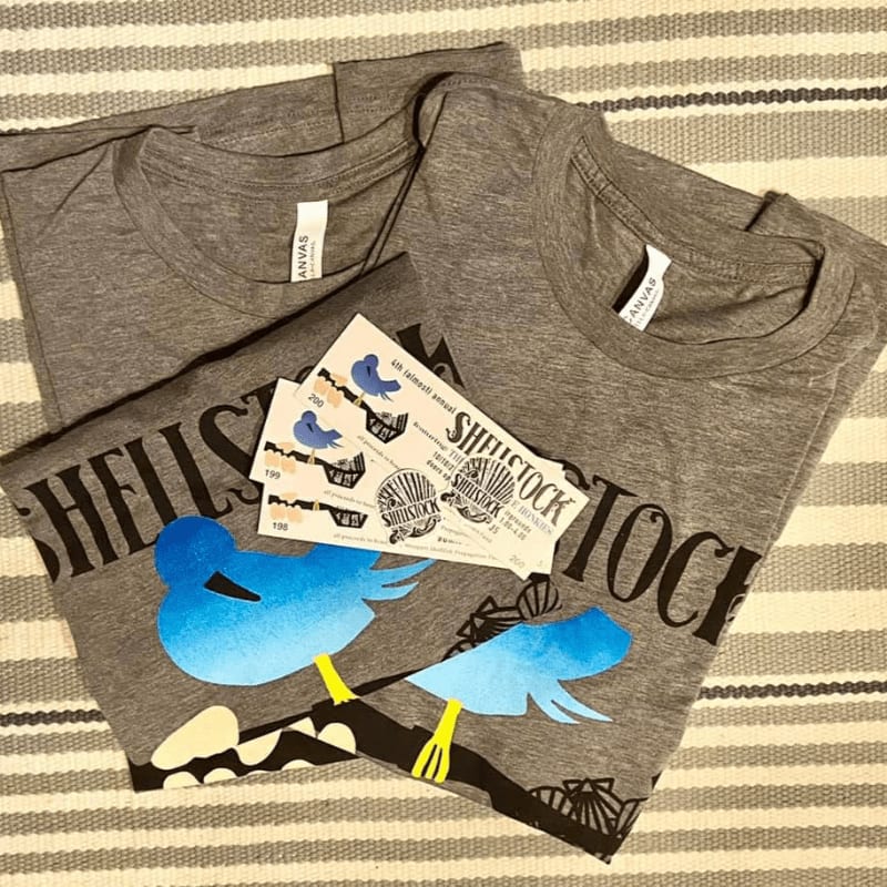 Two grey t-shirts with bird designs and stickers are laid out on a striped surface.