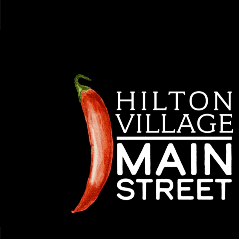 A red chili pepper stands to the left of white text that reads "HILTON VILLAGE MAIN STREET" against a black background.