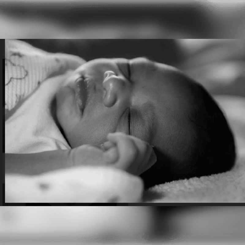 A newborn baby sleeps peacefully in the foreground, with a soft, blurred background.