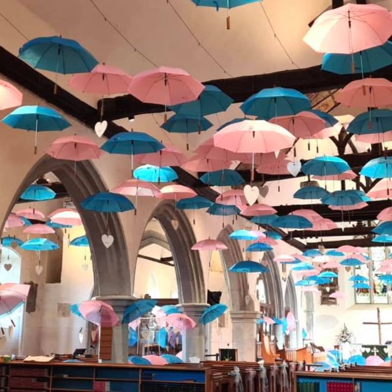 A ceiling adorned with numerous pink and blue umbrellas hangs above rows of bookshelves and arched architecture.