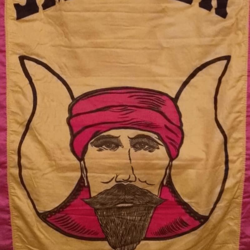 A yellow banner with a drawing of a man's face wearing a red turban and a dark mustache and beard is bordered by pink fabric.